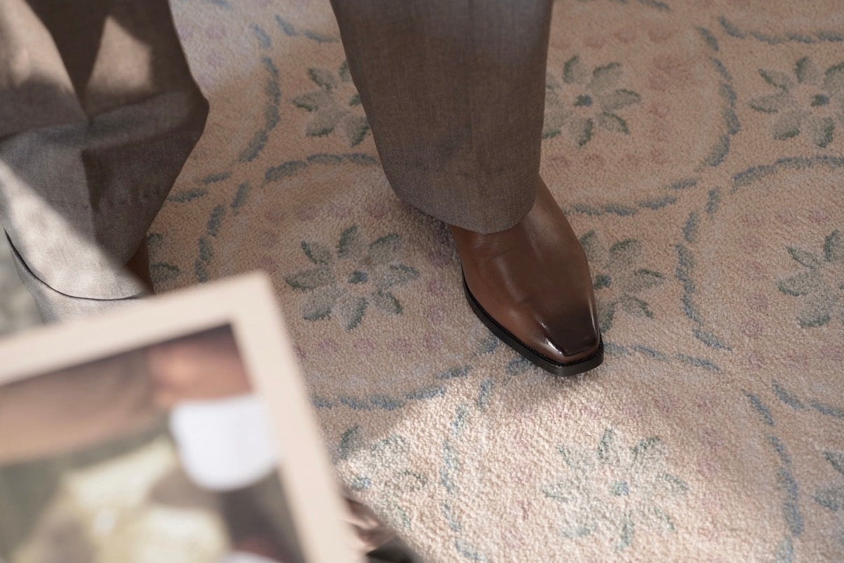 Person wearing brown shoes on a patterned carpet with a framed picture in the foreground.